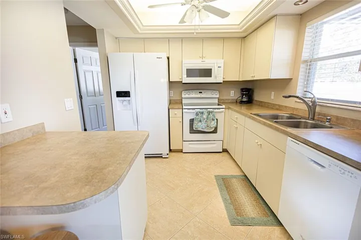 Kitchen with white appliances, cream cabinets, sink, ceiling fan, and kitchen peninsula