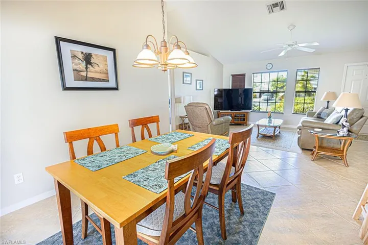 Dining room with light tile patterned floors, ceiling fan with notable chandelier, and vaulted ceiling