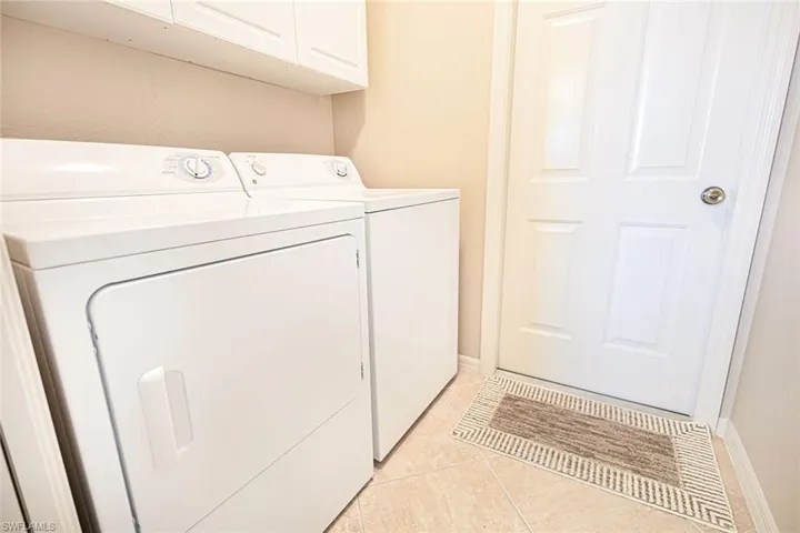 Laundry area with cabinets, light tile patterned floors, and washing machine and clothes dryer