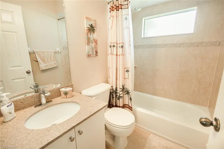 Full bathroom with tile patterned flooring, shower / bath combination with curtain, toilet, and vanity
