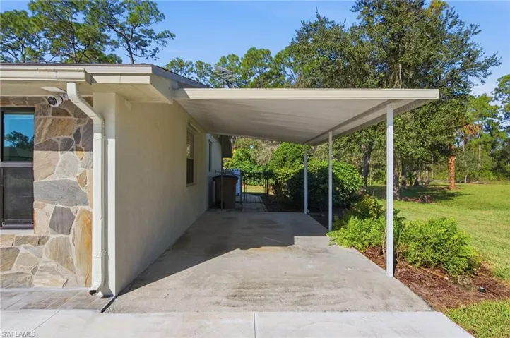 Exterior carport featuring a concrete parking pad, structural support columns, stone veneer siding, and surrounding landscape