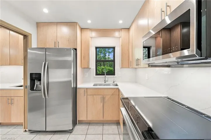 Kitchen featuring light-tone wood cabinetry, stone-finish countertops, stainless steel appliances, a tile backsplash, and recessed lighting