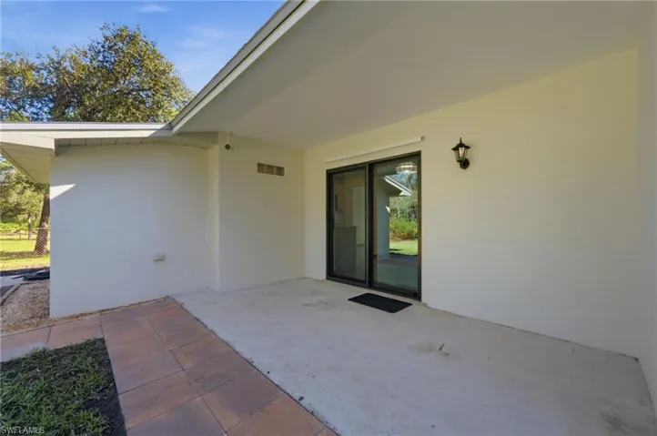 Covered concrete patio featuring tile accents, sliding glass doors, and exterior wall-mounted lighting