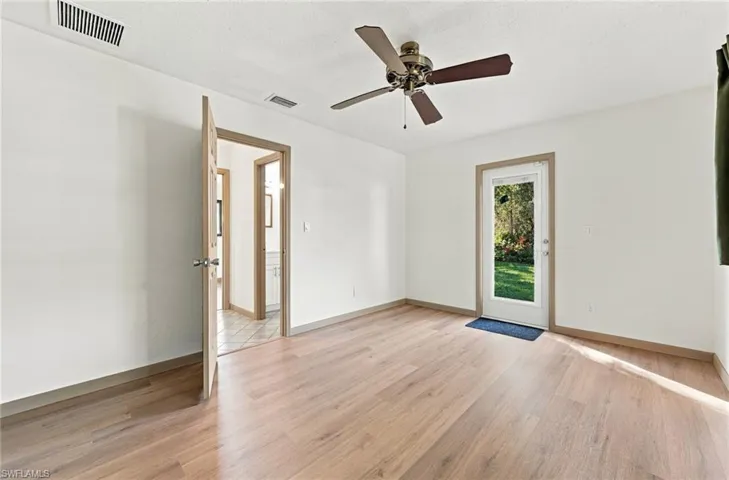 Bright, open room featuring warm wood-finish flooring, ceiling fan with brushed metal finish, French doors with natural wood frames, and abundant natural light from multiple glass door entries