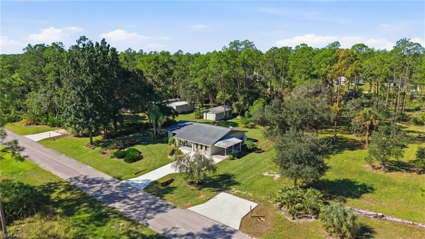Single-story residence featuring a paved driveway, covered front entryway, attached carport, and extensive surrounding green space with mature trees