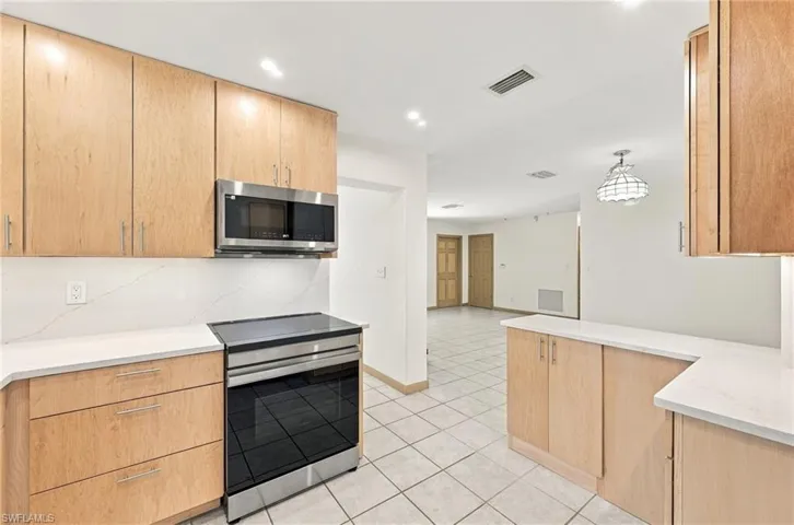 Kitchen featuring light wood-finish cabinetry, white stone-composite countertops, stainless steel microwave, and tile flooring
