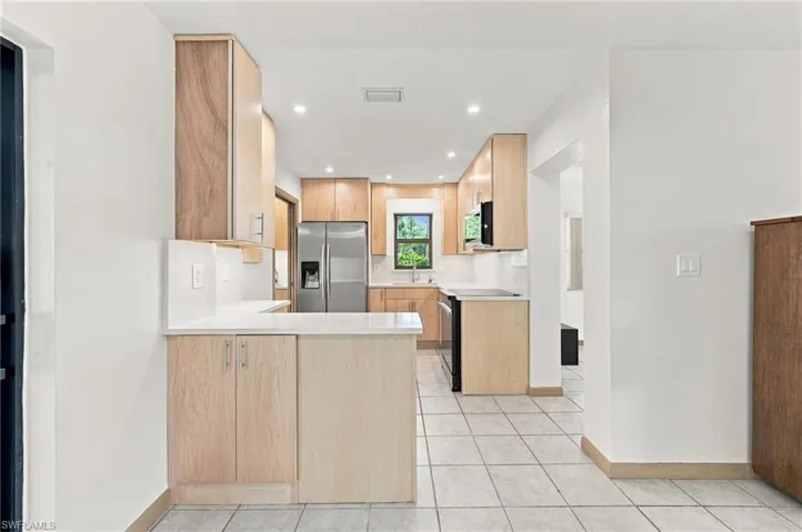 Kitchen featuring light wood-finish cabinetry, solid surface countertops, stainless steel appliances, recessed ceiling lighting, and tiled flooring