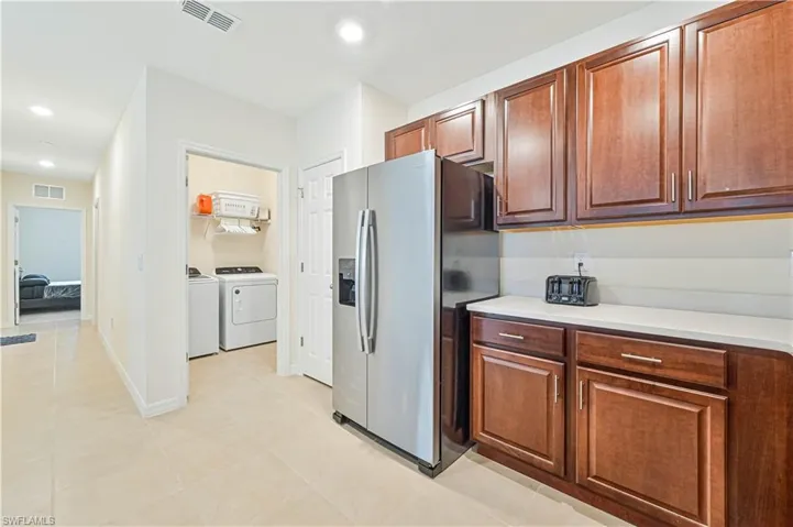 Kitchen with stainless steel fridge with ice dispenser, independent washer and dryer, and light tile patterned floors