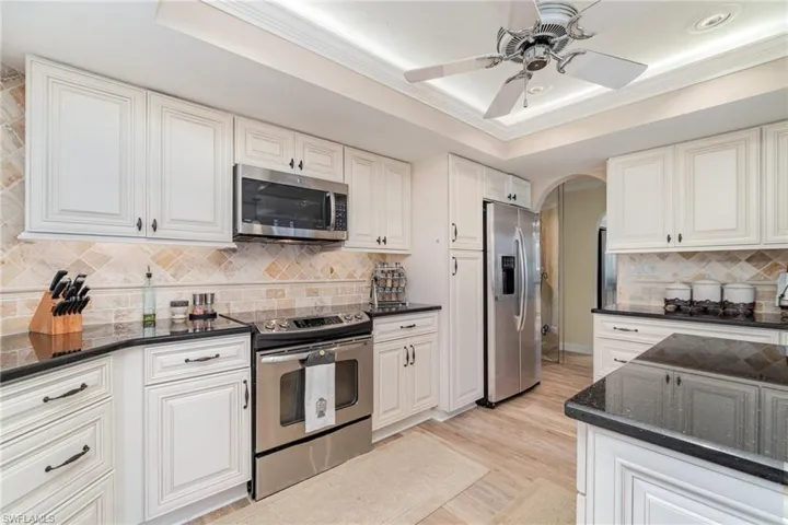 Kitchen with a raised ceiling, appliances with stainless steel finishes, backsplash, arched walkways, and ornamental molding