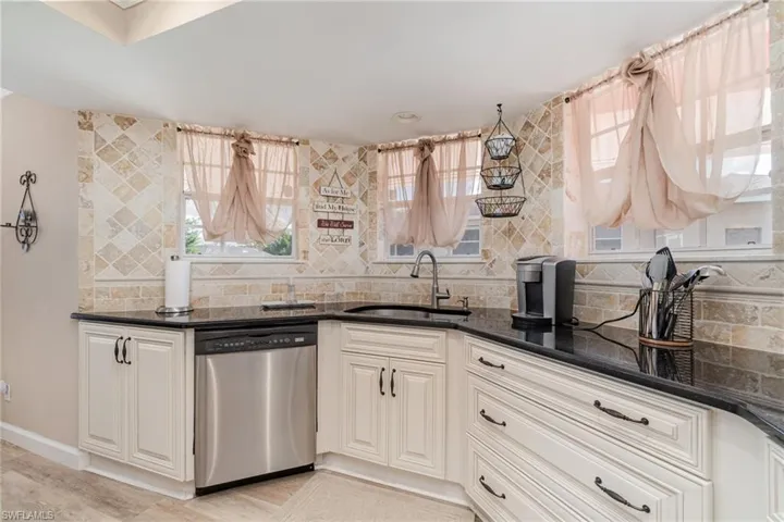 Kitchen with tasteful backsplash, dishwasher, dark stone counters, and light wood-style floors