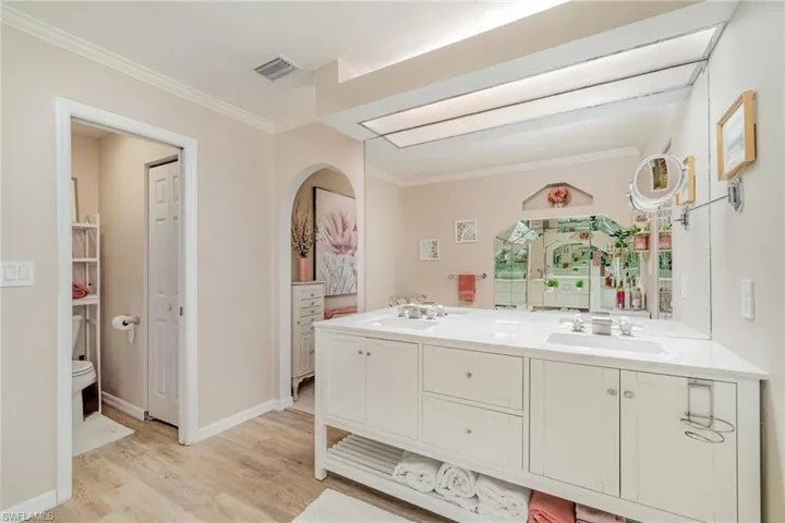 Bathroom featuring double vanity, ornamental molding, and light wood-style flooring