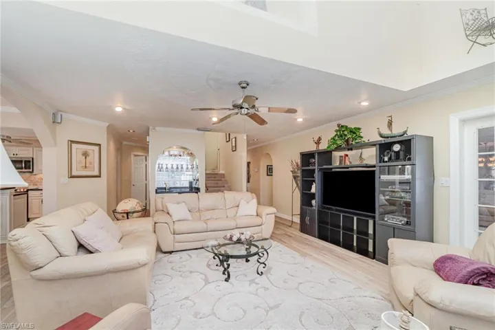 Living area with arched walkways, a ceiling fan, light wood-style flooring, recessed lighting, and crown molding