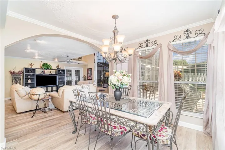 Dining room featuring ornamental molding, arched walkways, light wood-style flooring, a chandelier, and ceiling fan