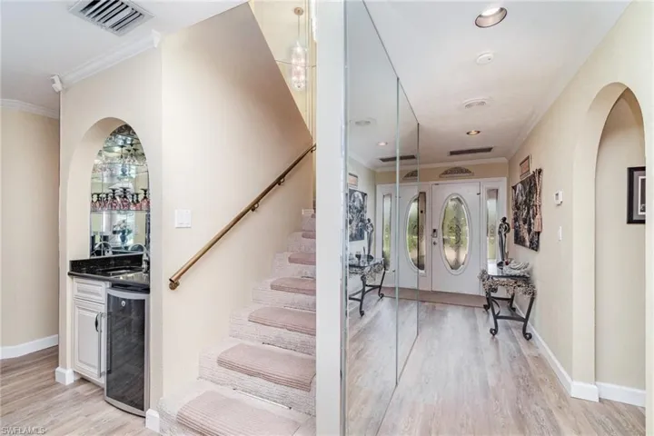 Foyer entrance with arched walkways, ornamental molding, light wood finished floors, wine cooler, and stairway