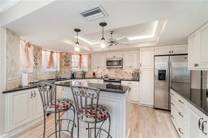 Kitchen with a raised ceiling, appliances with stainless steel finishes, light wood-style flooring, a kitchen breakfast bar, and hanging light fixtures