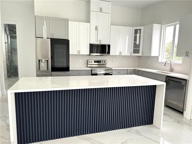 Kitchen with light marble finish flooring, light stone countertops, stainless steel appliances, glass insert cabinets, and gray cabinets
