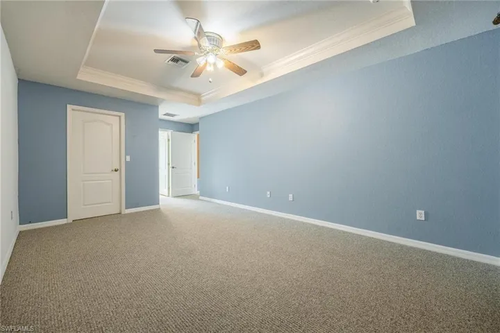 Carpeted empty room featuring ceiling fan, ornamental molding, and a tray ceiling