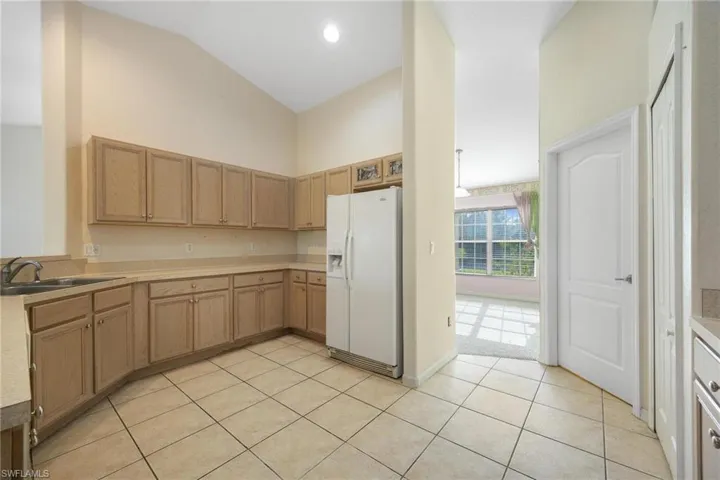 Kitchen featuring high vaulted ceiling, sink, white refrigerator with ice dispenser, and light tile patterned floors