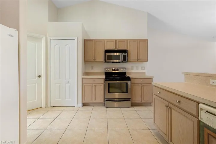 Kitchen featuring light tile patterned flooring, high vaulted ceiling, light brown cabinetry, and stainless steel appliances