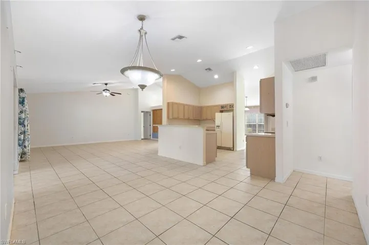 Kitchen with light tile patterned floors, hanging light fixtures, a kitchen island, and white refrigerator with ice dispenser