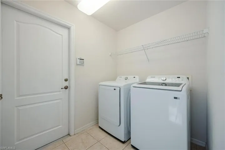 Washroom with washing machine and dryer and light tile patterned floors