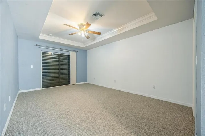 Carpeted empty room featuring ceiling fan and a raised ceiling