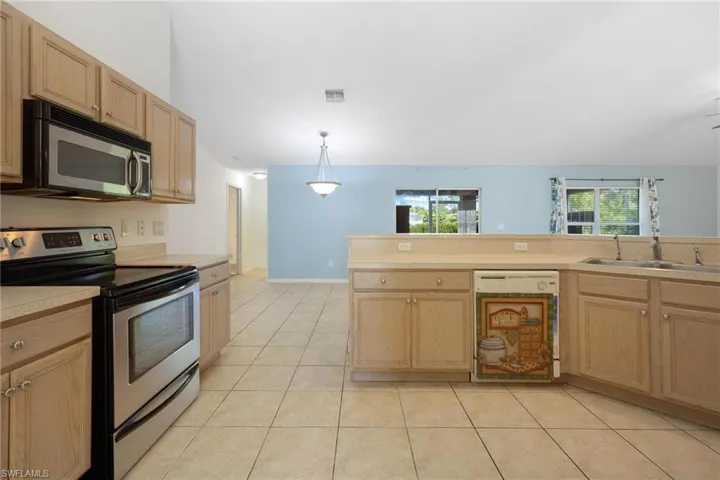 Kitchen with light tile patterned floors, appliances with stainless steel finishes, light brown cabinetry, decorative light fixtures, and sink