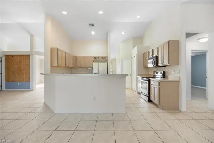 Kitchen with stainless steel appliances, light tile patterned floors, a kitchen island, light brown cabinetry, and a towering ceiling