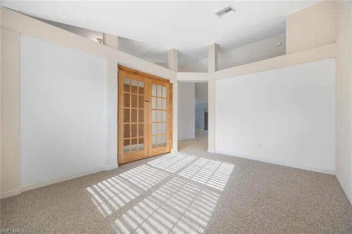 Carpeted spare room with french doors and high vaulted ceiling