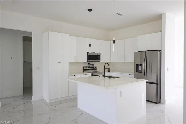 Kitchen featuring white cabinetry, stainless steel appliances, sink, and an island with sink