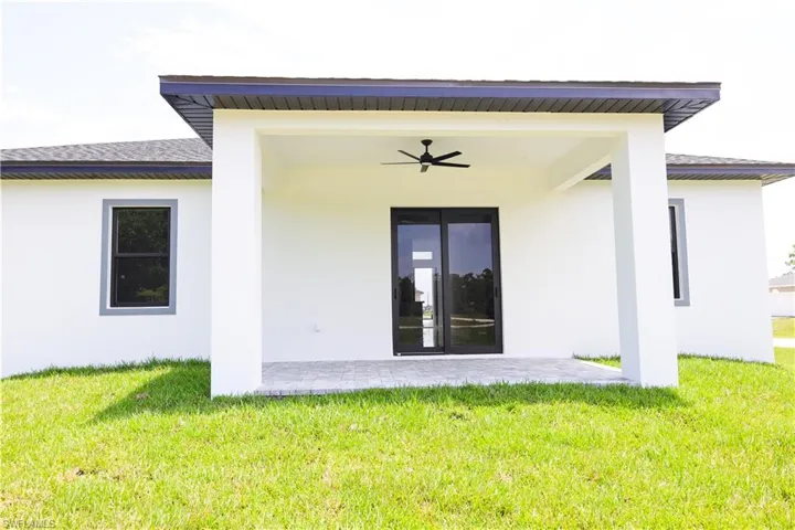 Rear view of property featuring ceiling fan, a patio area, and a lawn