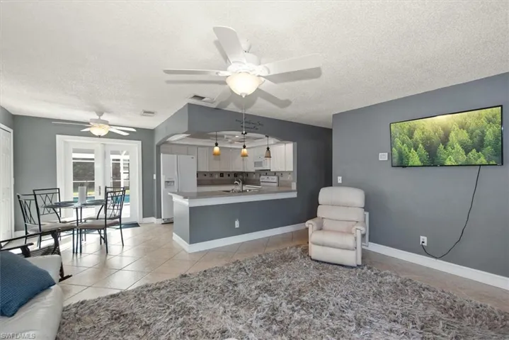 Living area with light tile patterned floors, ceiling fan, arched walkways, and a textured ceiling