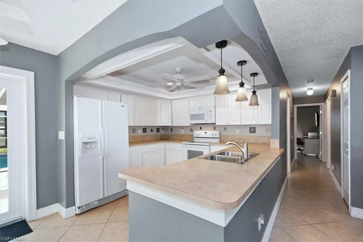 Kitchen with hanging light fixtures, white appliances, light tile patterned flooring, light countertops, and a textured ceiling