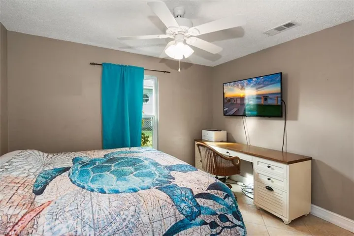 Bedroom featuring a textured ceiling, light tile patterned floors, ceiling fan, and a desk