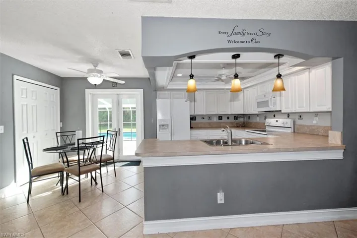 Kitchen featuring light tile patterned floors, light countertops, white cabinets, white appliances, and a textured ceiling