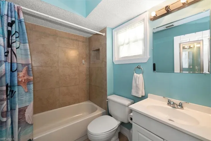 Bathroom with a textured ceiling, shower / tub combo with curtain, and vanity