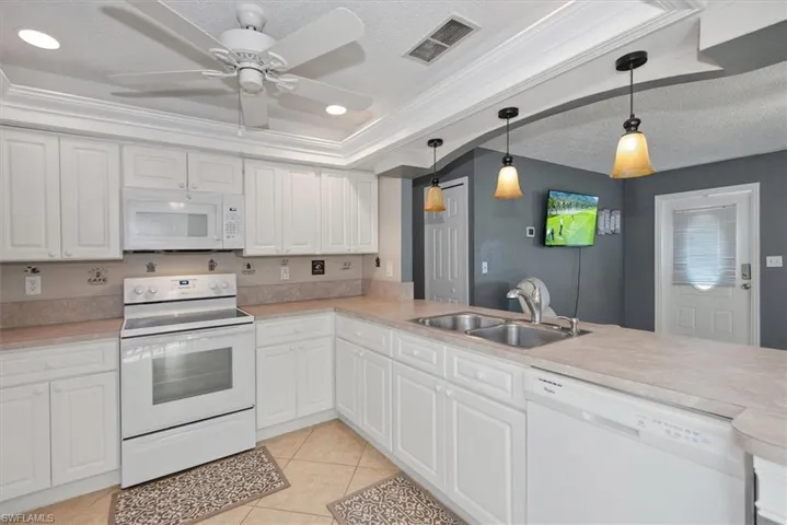 Kitchen featuring white appliances, light countertops, crown molding, white cabinets, and light tile patterned floors