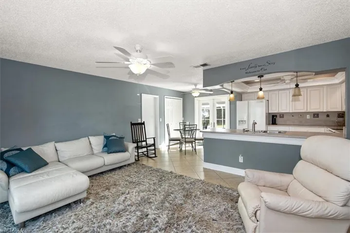 Living room featuring a textured ceiling, light tile patterned flooring, ceiling fan, and a raised ceiling