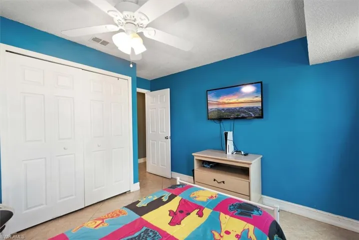 Bedroom featuring a textured ceiling, light tile patterned floors, a closet, and ceiling fan