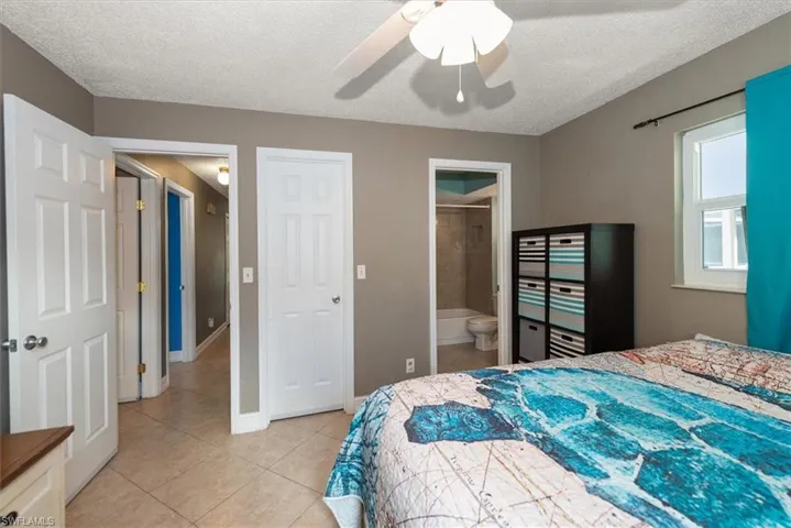 Bedroom with a textured ceiling, light tile patterned flooring, ceiling fan, and ensuite bath