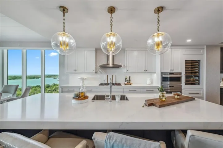 Kitchen featuring a breakfast bar area, light stone counters, hanging light fixtures, a water view, and recessed lighting