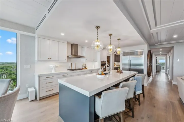 Kitchen with white cabinetry, hanging light fixtures, a breakfast bar, appliances with stainless steel finishes, and a kitchen island with sink