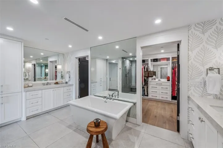 Bathroom with a walk in closet, two vanities, wallpapered walls, a soaking tub, and light tile patterned flooring