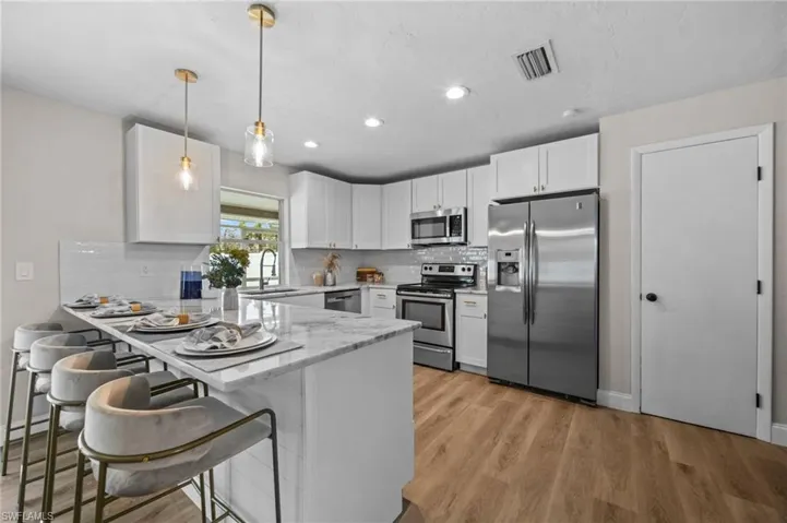 Kitchen featuring a breakfast bar, stainless steel appliances, sink, decorative light fixtures, and white cabinets