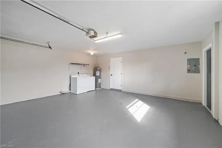 Garage featuring electric panel, a garage door opener, washing machine and clothes dryer, and electric water heater