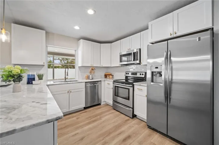 Kitchen with sink, decorative light fixtures, light stone counters, white cabinetry, and stainless steel appliances