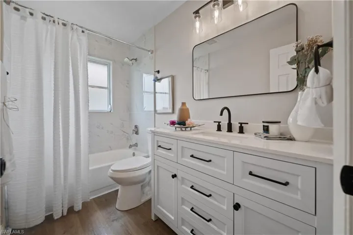 Full bathroom with toilet, shower / tub combo with curtain, vanity, and wood-type flooring