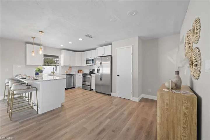 Kitchen featuring a breakfast bar area, stainless steel appliances, hanging light fixtures, kitchen peninsula, and white cabinets