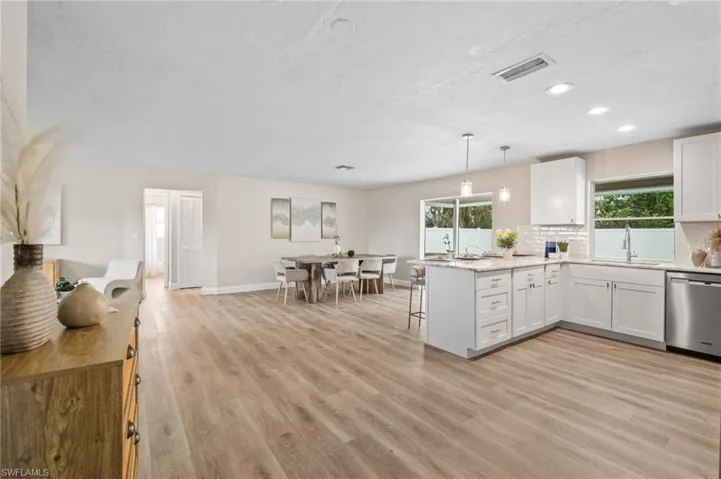 Kitchen featuring sink, kitchen peninsula, stainless steel dishwasher, decorative light fixtures, and white cabinetry
