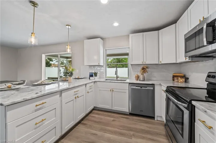 Kitchen with sink, stainless steel appliances, light stone counters, decorative light fixtures, and white cabinets